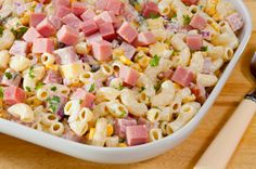 a white bowl filled with pasta and vegetables on top of a table next to a wooden spoon