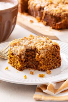 a piece of carrot cake on a plate with a fork and cup of coffee in the background