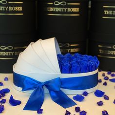 blue roses are in a white box with a bow on the table next to black pails