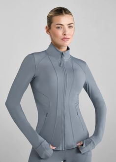 a woman in grey bodysuit with her hands on her hips, posing for the camera