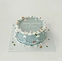 a blue birthday cake with white frosting and flowers on it's side, sitting on a card