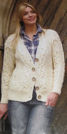 a woman standing in front of a wooden door wearing a white sweater and cardigan