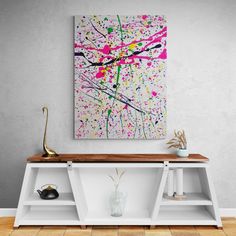 an abstract painting hangs on the wall above a white shelf