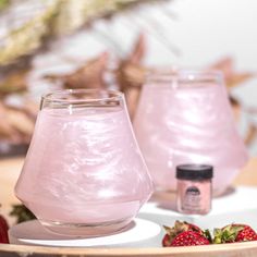 two glass vases sitting on top of a table with strawberries in front of them