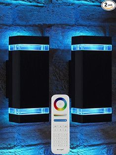 two speakers and a remote control in front of a brick wall with blue lights on it