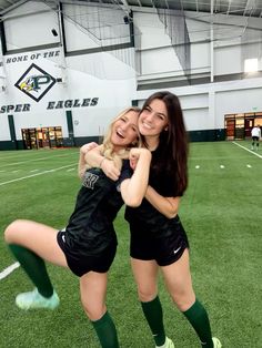 two young women are posing for a photo in the middle of an indoor soccer field