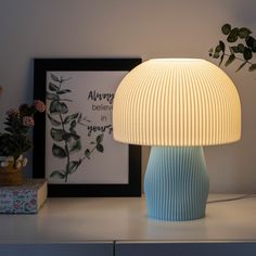 a blue lamp sitting on top of a white table next to a vase with flowers