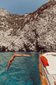 a man dives into the water from a boat in front of a rocky cliff