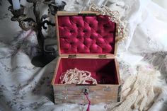 an open wooden box with pearls inside sitting on a bed next to a candle holder