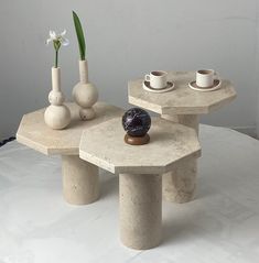 two tables with cups and vases sitting on top of each other in front of a white wall