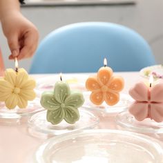 a person lighting candles with small flowers on top of the candle holders in front of them