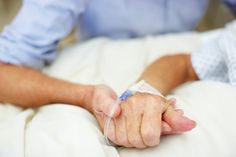 an older person holding the hand of another person in hospital bed with ivs attached to their arm