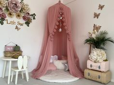 a pink canopy bed sitting next to a white table and chair in a room with flowers on the wall