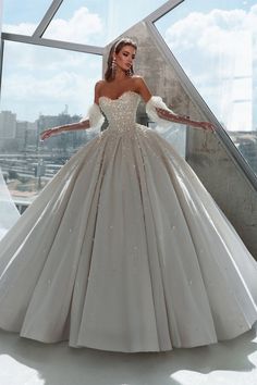 a woman in a wedding dress standing by a window with her arms out and hands on her hips