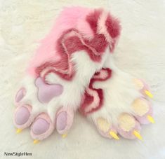 a pink and white furry animal paw with yellow spikes on it's claws, laying on a white fur surface