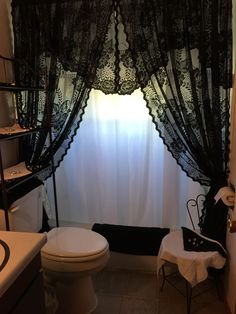 a white toilet sitting next to a bath tub under a black sheer curtain in a bathroom