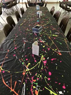 a long table covered in black cloth with colorful paint splattered on it