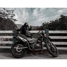 a man sitting on the back of a motorcycle next to a wooden fence with trees in the background