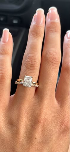 a woman's hand with a diamond ring on her left and a car dashboard in the background