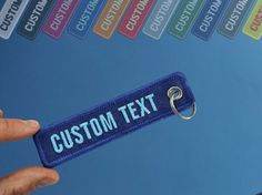 a hand holding a keychain with the word custom text on it in front of a blue background