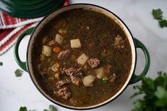 a pot filled with meat and potatoes sitting on top of a counter next to some parsley