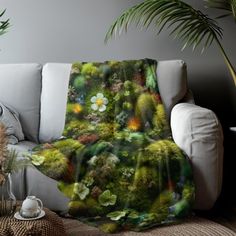 a couch with a blanket on it that is covered in plants and flowers, sitting next to a potted plant