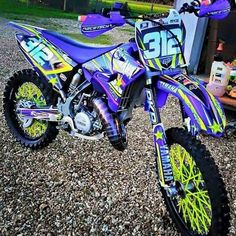 a purple dirt bike parked on top of a gravel covered field next to a building