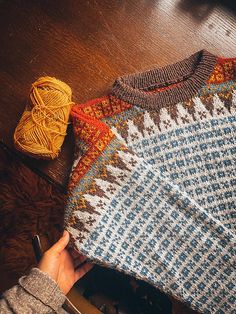 someone is holding up a sweater on the floor next to some knitting needles and yarn