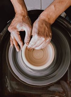 two hands on a potter's wheel making something out of clay with his fingers