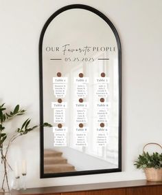 a wedding seating chart is displayed on a mirror above a dresser with potted plants