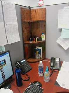 an office desk with a phone, laptop and water bottle on it in front of a bookshelf