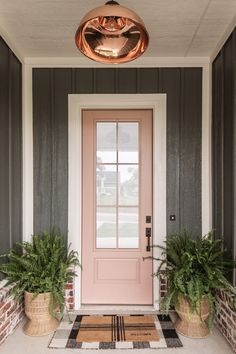 a pink front door with two planters on the side and a light fixture above it