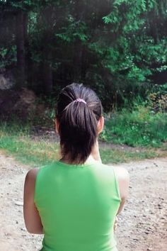 a woman in a green shirt is sitting on a dirt road and looking at the woods