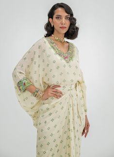 This elegant Ivory Embroidered Toga Cape Skirt Set is a timeless blend of sophistication and comfort. Crafted from soft crepe fabric, the set features a Ivory-colored, loose-fitting cape adorned with intricate floral embroidery around the neckline and cuffs. Paired with a wrap-style skirt that accentuates the waist and drapes effortlessly, it creates a flattering fit while ensuring easy movement. Ideal Indo-Western attire for home poojas, family gatherings, or festive occasions. Composition : Top and Skirt - Crepe Care: Dry Clean Only and Vacuum Storage This product can be customized for sleeves, blouse length and neckline Delivery : 4-6 weeks as the product is hand crafted. Check Size Guide or choose MySize for free customisation (All Sizes above XL can be made at 15% additional cost) For White Silk Kaftan For Festive Occasions, White Embroidered Silk Kaftan, White Silk Embroidered Kaftan, Cream Georgette Sets With Floral Embroidery, White Summer Sets For Reception, White Sets For Summer Reception, Summer White Reception Sets, White Summer Reception Sets, Elegant White Kaftan With Pearl Embroidery