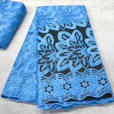 two pieces of blue and black lace on a white tablecloth, one with an intricate design