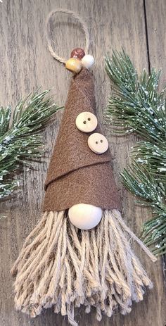 a christmas ornament made out of yarn and buttons on a wooden surface with pine branches