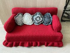 a red crocheted couch with three flowers on the back and one flower in the middle