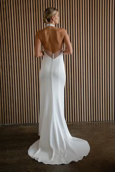 the back of a woman in a white wedding dress standing against a striped wall with her hands on her hips