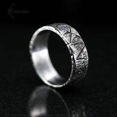 a wedding ring with an intricate design on the outside and inside, sitting on a black surface