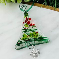 a glass christmas tree ornament hanging on a table with green and red decorations