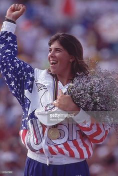 an olympic medal winning woman holding flowers in her hand and the usa flag on her shoulders