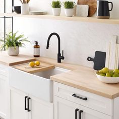 a kitchen with white cabinets and black faucet, wooden cutting board on the counter