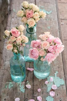 three vases filled with pink and white flowers sitting on a wooden table next to confetti