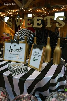 a table topped with black and white candy bar signs next to bottles of wine on top of a striped table cloth