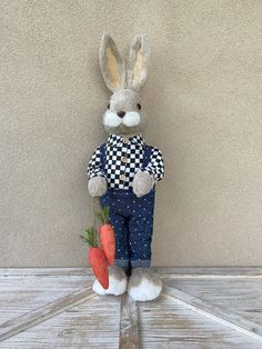 a stuffed rabbit holding two carrots on a fork in front of a beige wall