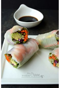 four rolls on a white plate with dipping sauce