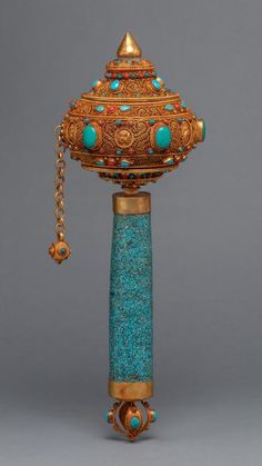 an ornate gold and turquoise colored object with chains hanging from it's sides on a gray background