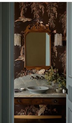 a bathroom sink sitting under a mirror next to a wall papered with flowers and leaves