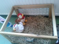 two stuffed animals sitting in a caged area with hay and chicken wire on the floor