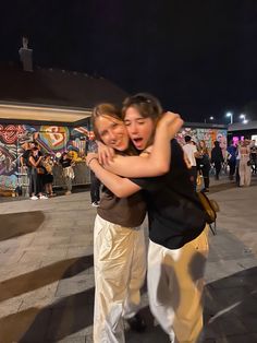 two people hugging each other in front of a building with graffiti on the wall behind them